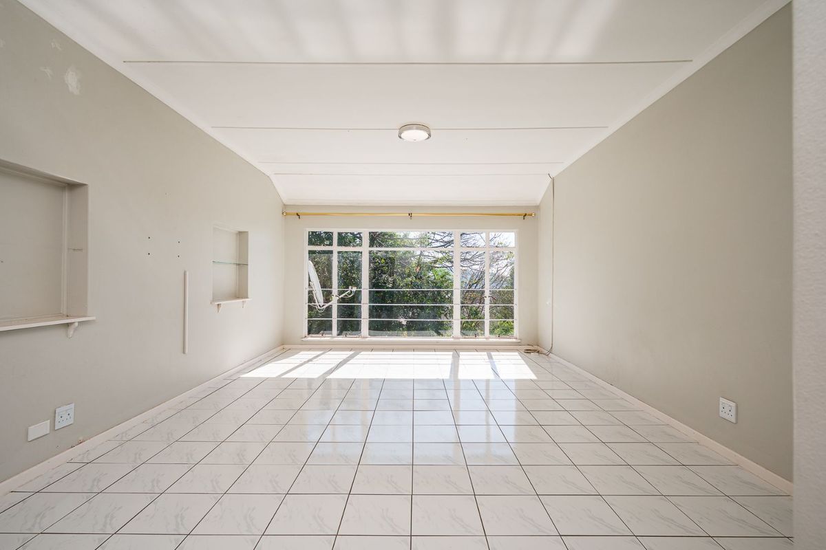 A bright, empty living room featuring white tiled flooring, large windows with natural light, and built-in wall shelving.