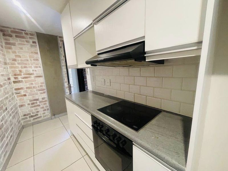 Modern kitchen featuring white cabinetry, subway tile backsplash, stone countertops, and integrated appliances including an electric hob and oven.