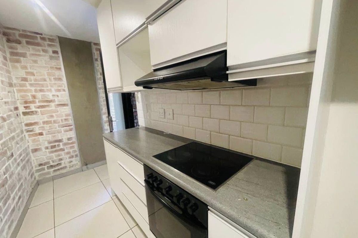 Modern kitchen featuring white cabinetry, subway tile backsplash, stone countertops, and integrated appliances including an electric hob and oven.