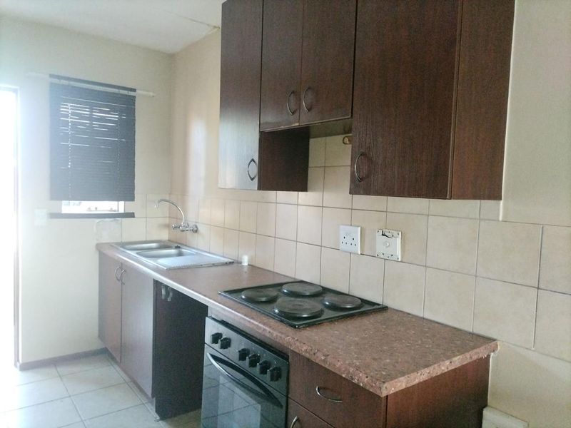 A functional kitchen featuring dark wood cabinetry, laminate countertops, a built-in oven and hob, and tiled splashbacks.