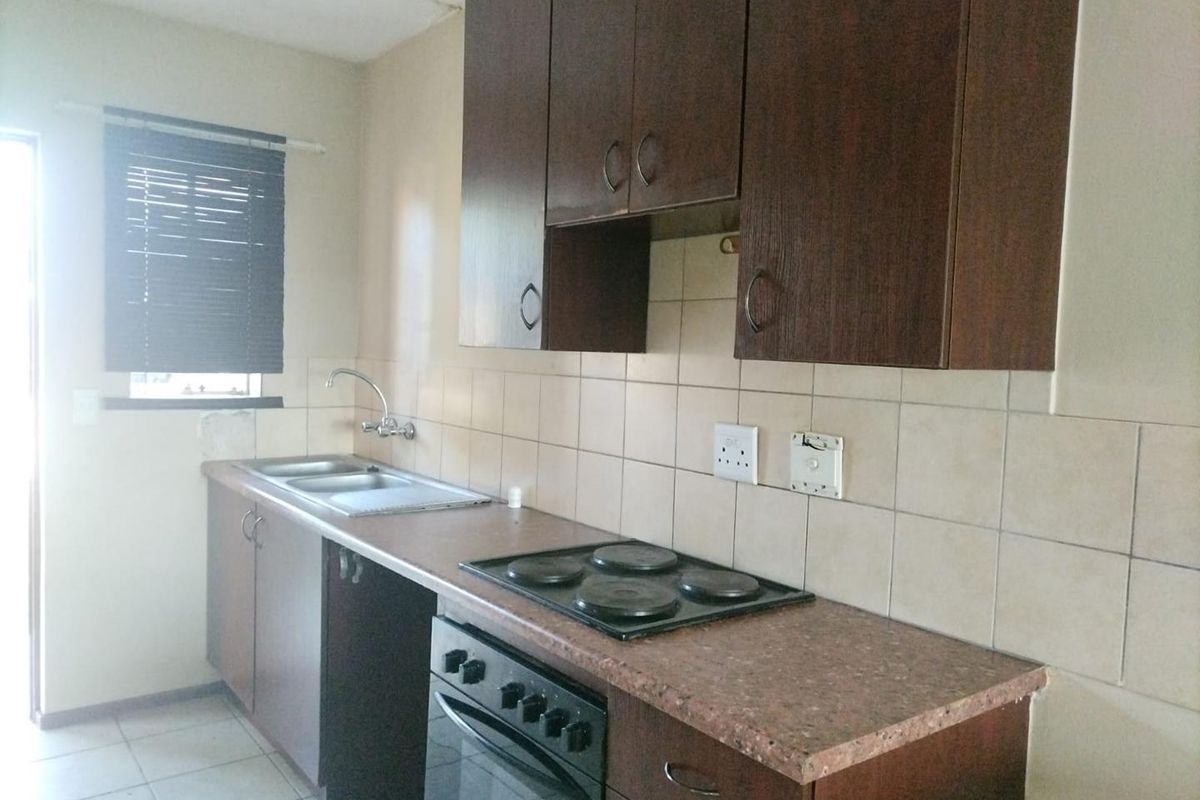 A functional kitchen featuring dark wood cabinetry, laminate countertops, a built-in oven and hob, and tiled splashbacks.