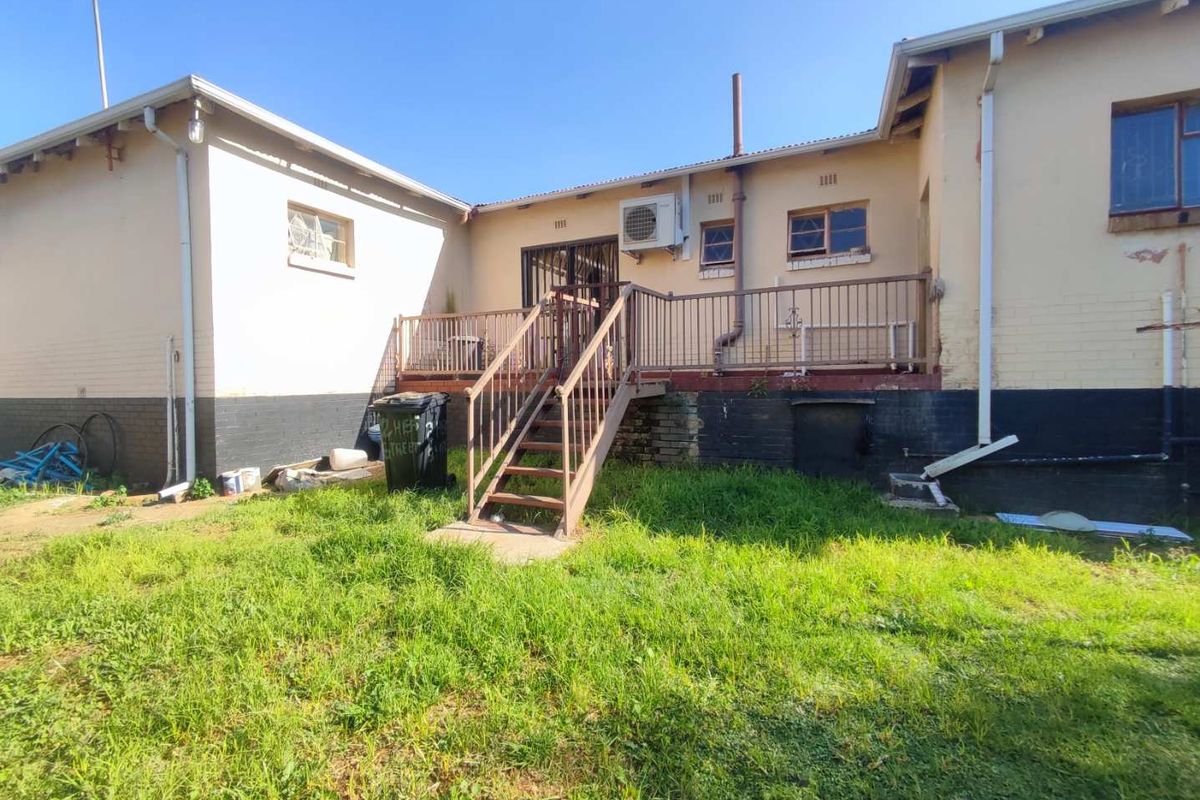Rear view of the property featuring a raised deck with metal railings, external air conditioning unit, and an expansive backyard area.