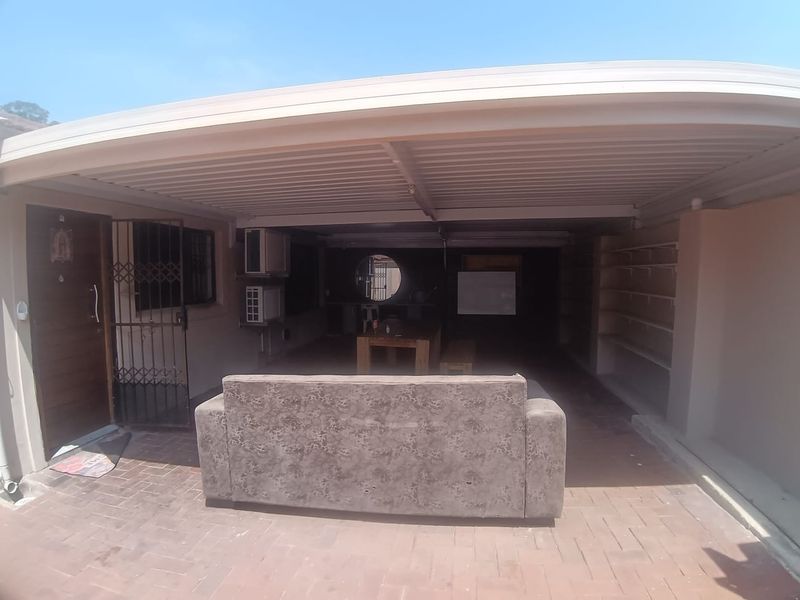 A covered outdoor patio area featuring paved flooring, built-in shelving, and a security gate, providing a functional space for outdoor living.