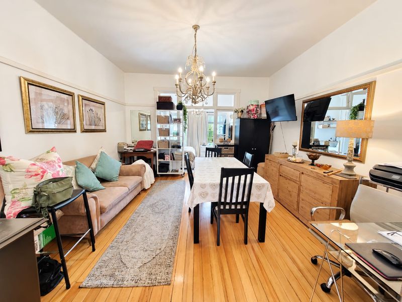 Spacious open-plan living and dining area featuring polished hardwood flooring, classic picture rails, and a decorative chandelier, leading to bright french doors.