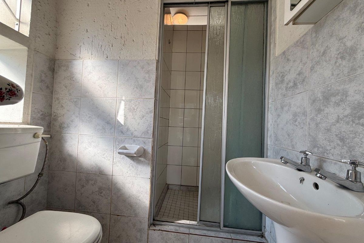A dated bathroom featuring a pedestal basin, toilet, and a separate shower enclosure with sliding doors, requiring cosmetic updates to modernize the space.