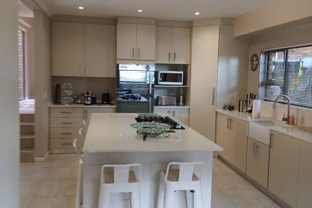 Modern kitchen featuring a central island with a built-in gas hob, stone countertops, ample cabinetry, and integrated appliances, finished with neutral floor tiles.