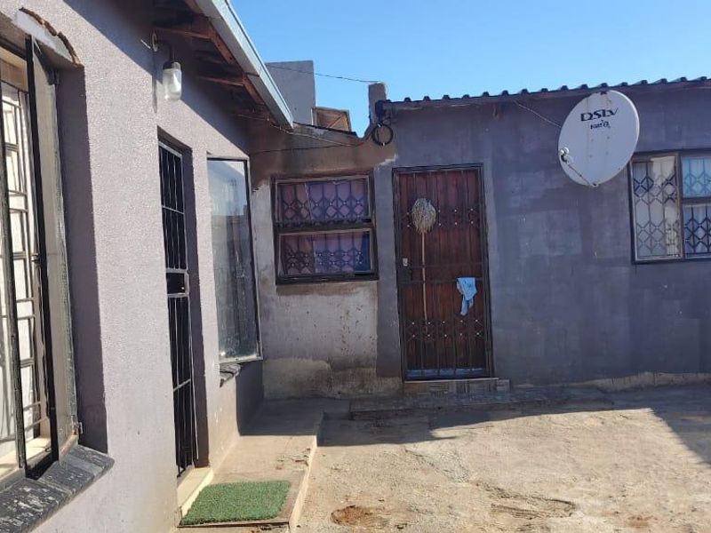 Rear exterior view of the property featuring concrete paving, security bars on windows, and a satellite dish mounted on the wall.