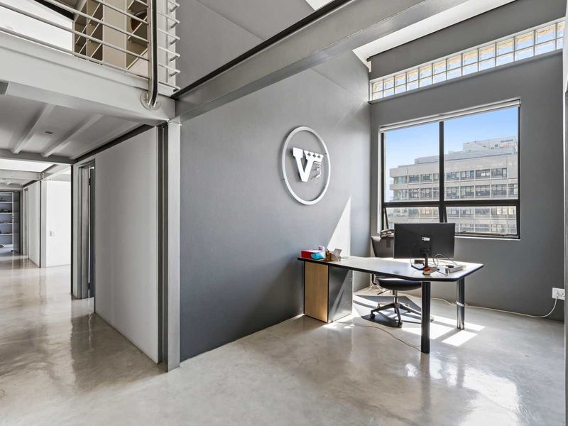 Modern office space featuring polished concrete floors, exposed steel structural elements, and a mezzanine level with abundant natural light from large windows.