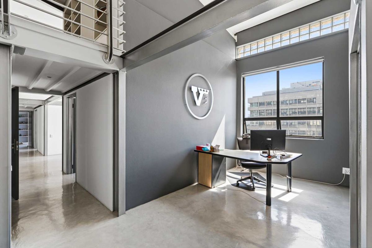Modern office space featuring polished concrete floors, exposed steel structural elements, and a mezzanine level with abundant natural light from large windows.