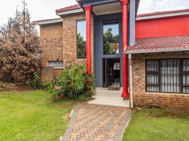 Front elevation of a face brick house featuring a paved walkway, decorative red columns, and a tiled roof.