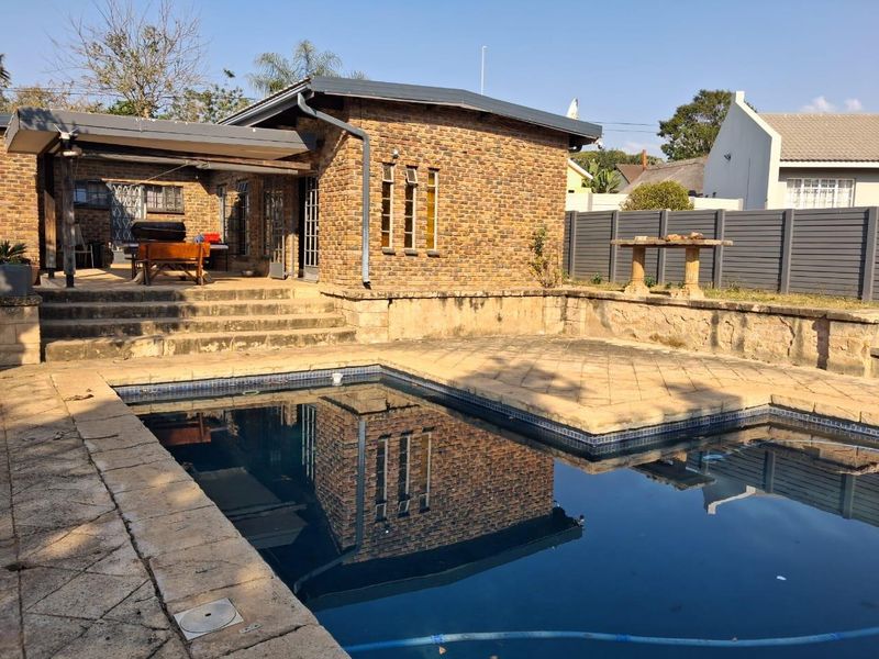 Outdoor pool area featuring a swimming pool, stone paved surround, covered patio space, and brick exterior wall with a retaining wall structure.