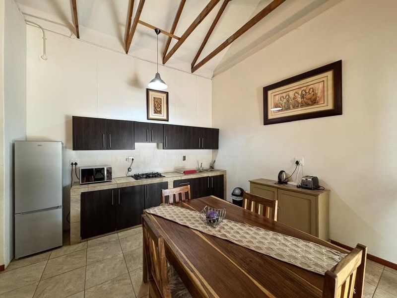 Open-plan kitchen and dining area featuring tiled floors, exposed timber roof trusses, and dark wood cabinetry with integrated gas hob and sink.
