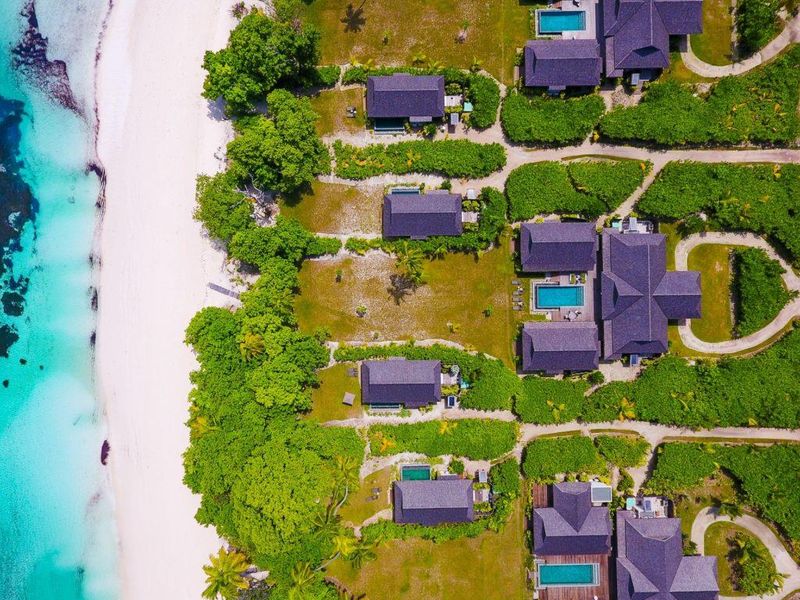 Aerial view of a luxury villa resort featuring multiple private swimming pools, lush landscaped gardens, and direct access to a pristine white sand beach.