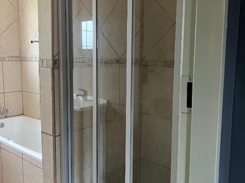 A functional bathroom featuring a bathtub, a separate shower enclosure with sliding doors, and a pedestal basin with neutral ceramic tiling.