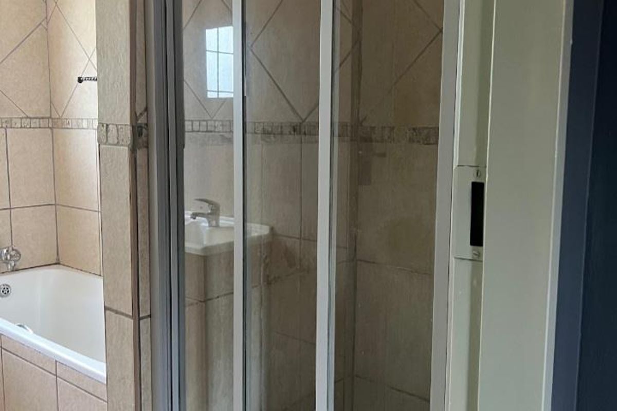 A functional bathroom featuring a bathtub, a separate shower enclosure with sliding doors, and a pedestal basin with neutral ceramic tiling.