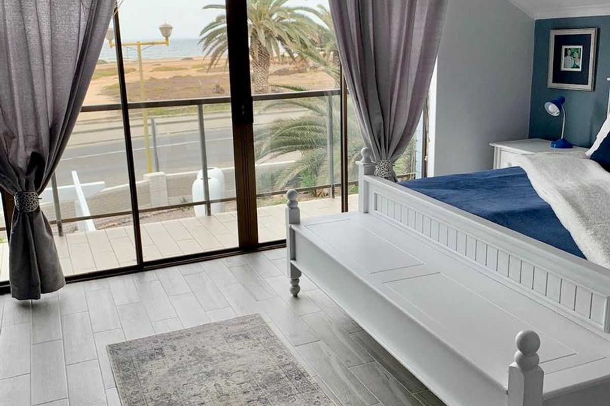 A bright bedroom featuring wood-look tile flooring, a vaulted ceiling, and large sliding glass doors opening onto a balcony with coastal views.