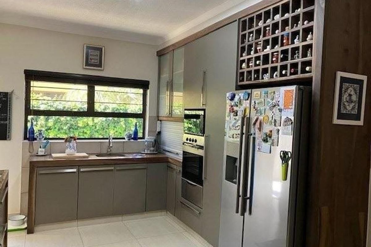 Modern kitchen featuring sleek grey cabinetry, built-in oven, integrated microwave, wine rack, and a window overlooking the garden.