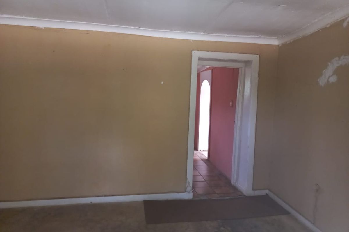 An empty living room space featuring plain walls and coving, requiring cosmetic updates and repairs to the wall surfaces and flooring.