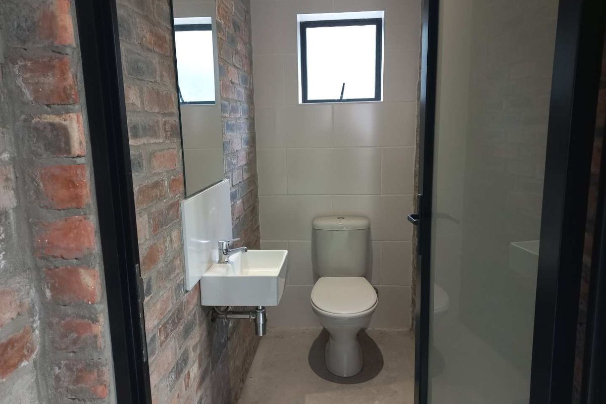 A modern bathroom featuring exposed brick walls, a wall-mounted basin, a toilet, and a small window, finished with contemporary black door frames.