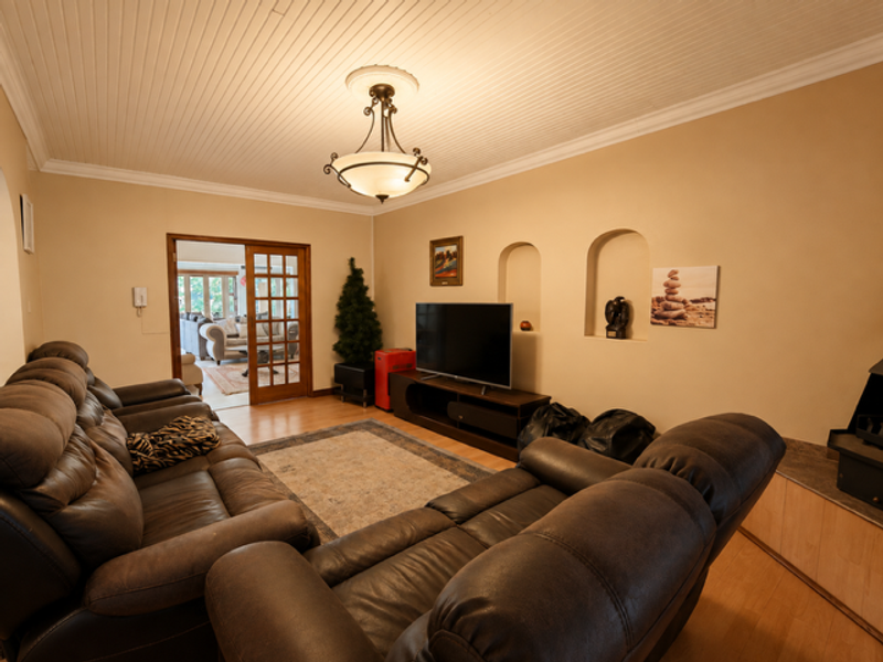 A comfortable living room featuring a beadboard ceiling, crown molding, and decorative wall niches, with French doors leading to an adjacent living space.