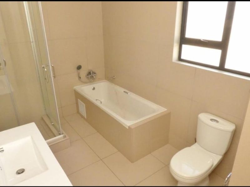 A clean, modern bathroom featuring a built-in bathtub, separate glass shower enclosure, vanity basin, and toilet with neutral floor-to-ceiling tiling.