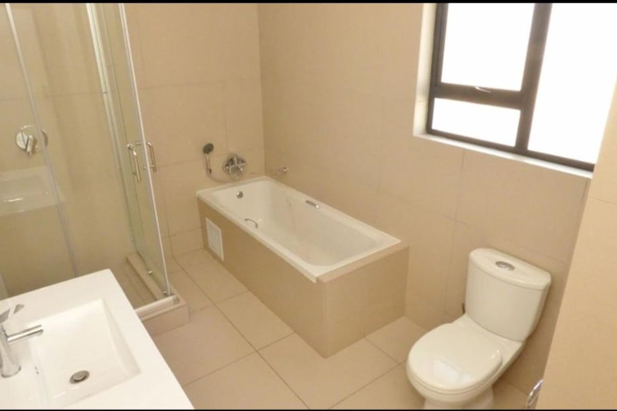 A clean, modern bathroom featuring a built-in bathtub, separate glass shower enclosure, vanity basin, and toilet with neutral floor-to-ceiling tiling.