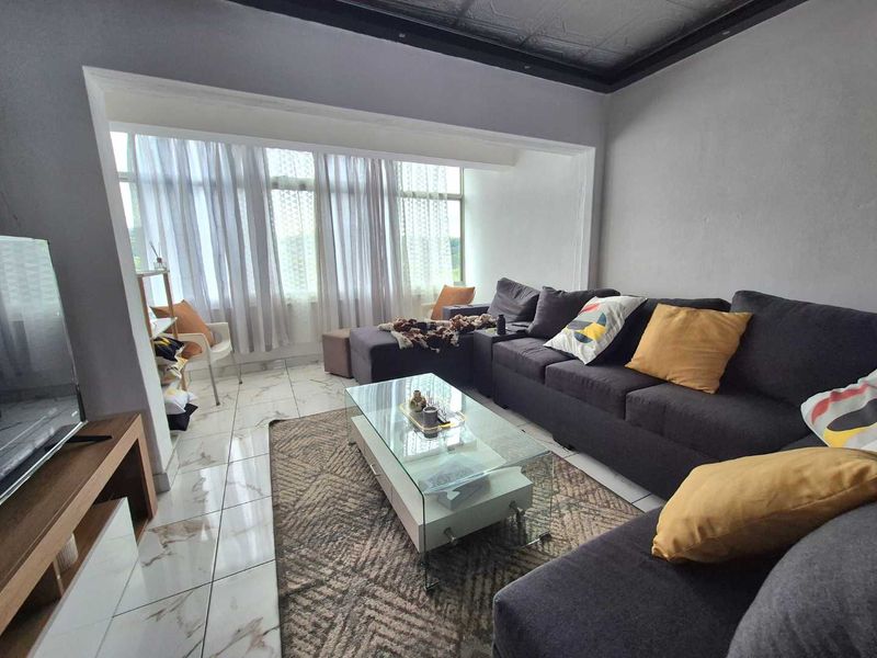 A living room featuring marble-look tiled flooring and a recessed ceiling, with large windows providing natural light.