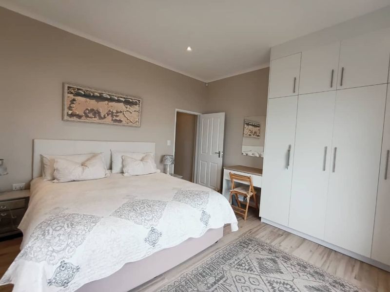 A well-maintained bedroom featuring laminate flooring, recessed lighting, and a large floor-to-ceiling built-in wardrobe with an integrated vanity area.