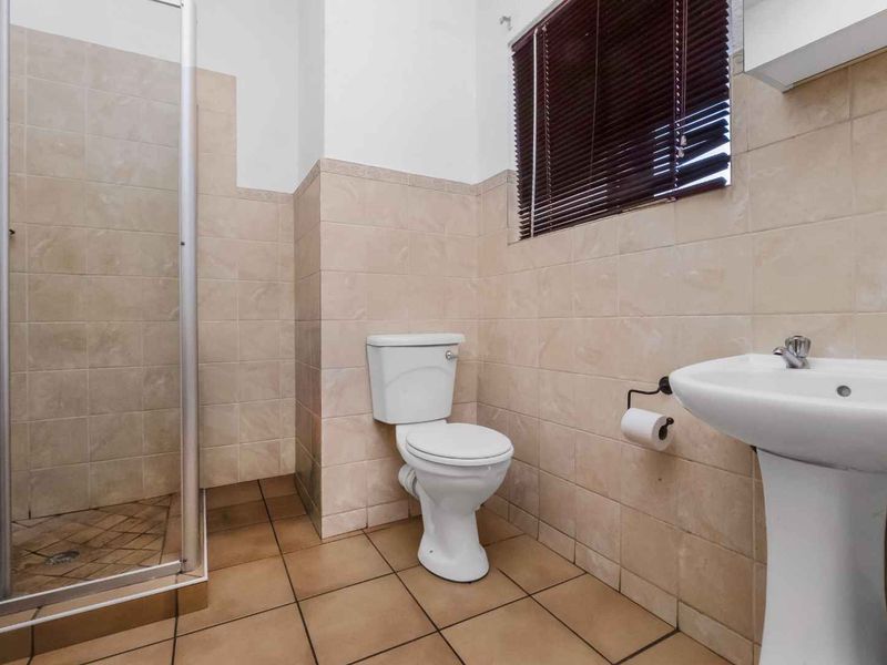 A functional bathroom featuring a shower enclosure, pedestal basin, and toilet with neutral wall and floor tiling.