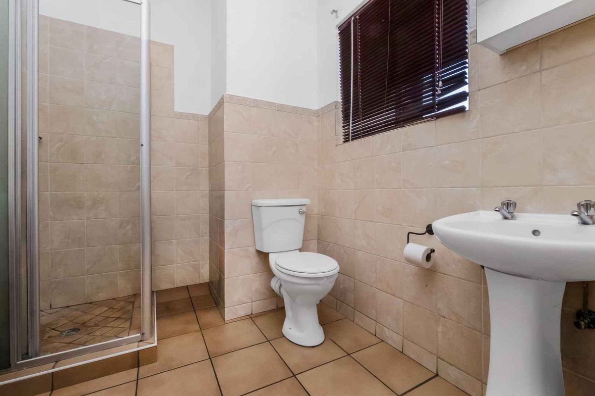 A functional bathroom featuring a shower enclosure, pedestal basin, and toilet with neutral wall and floor tiling.