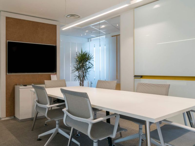A modern, well-lit office meeting room featuring a glass partition, built-in whiteboard, and cork wall detailing, suitable for professional collaboration.