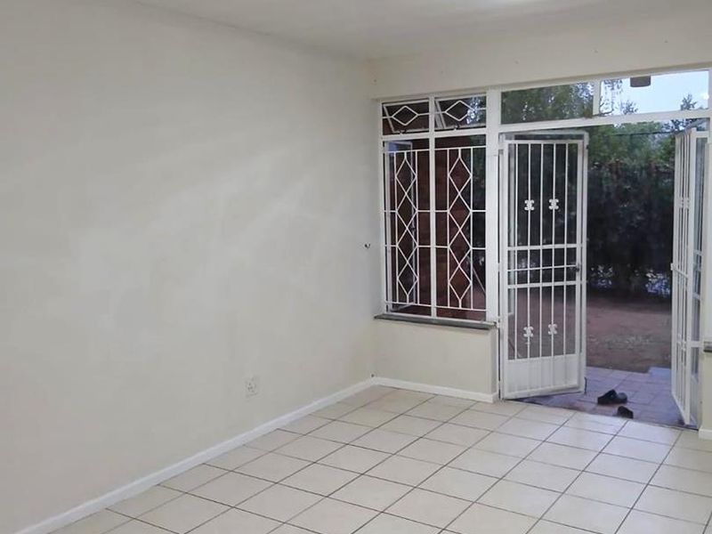 An empty living room featuring neutral tiled flooring, security bars on the windows, and a security gate leading to the outdoor area.