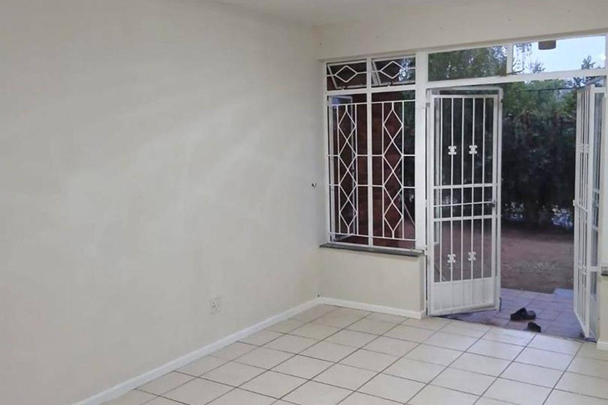 An empty living room featuring neutral tiled flooring, security bars on the windows, and a security gate leading to the outdoor area.
