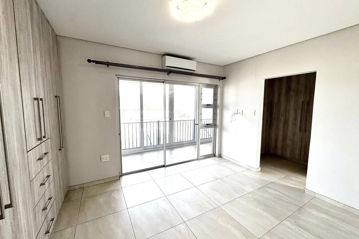 A bright bedroom featuring tiled flooring, built-in cabinetry, a wall-mounted air conditioning unit, and sliding glass doors leading to a balcony.
