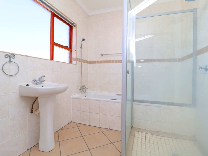 A functional bathroom featuring a pedestal basin, a bathtub, and a separate shower enclosure with tiled walls and flooring.