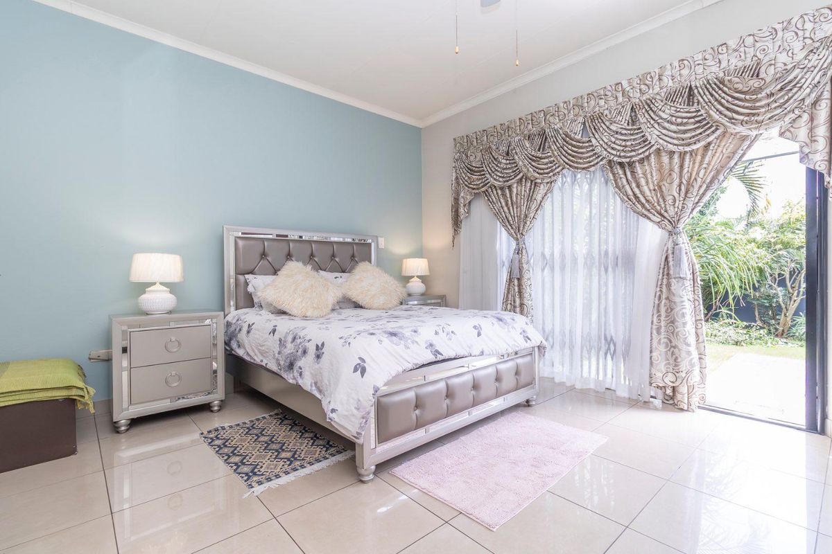 A bright bedroom featuring tiled flooring, a light blue accent wall, and large sliding glass doors providing direct access to the garden.