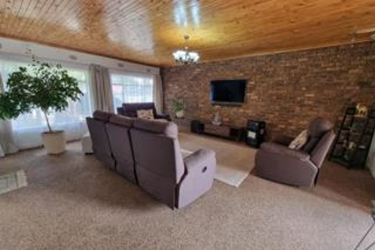 Spacious living room featuring a prominent exposed brick wall and a warm timber-paneled ceiling, offering a cozy and character-filled atmosphere.