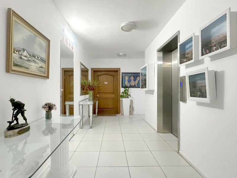 A well-maintained apartment hallway featuring tiled flooring, a stainless steel elevator entrance, and a solid wood front door.