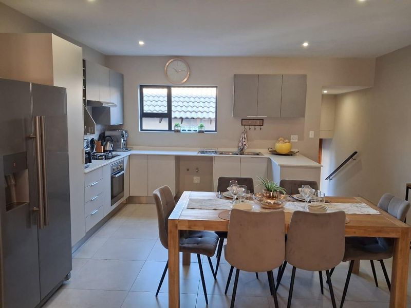 Modern open-plan kitchen and dining area featuring sleek cabinetry, stone countertops, integrated appliances, and tiled flooring, seamlessly connected to the staircase.