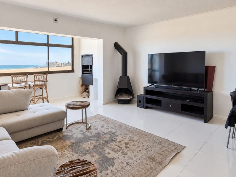 Spacious open-plan living area featuring a built-in fireplace, indoor braai, and large windows with direct ocean views and tiled flooring throughout.