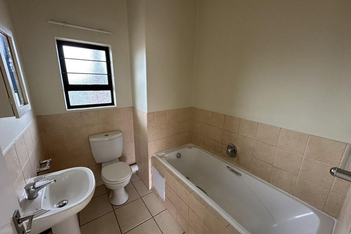 A functional bathroom featuring a pedestal basin, toilet, and bathtub with neutral wall and floor tiling.