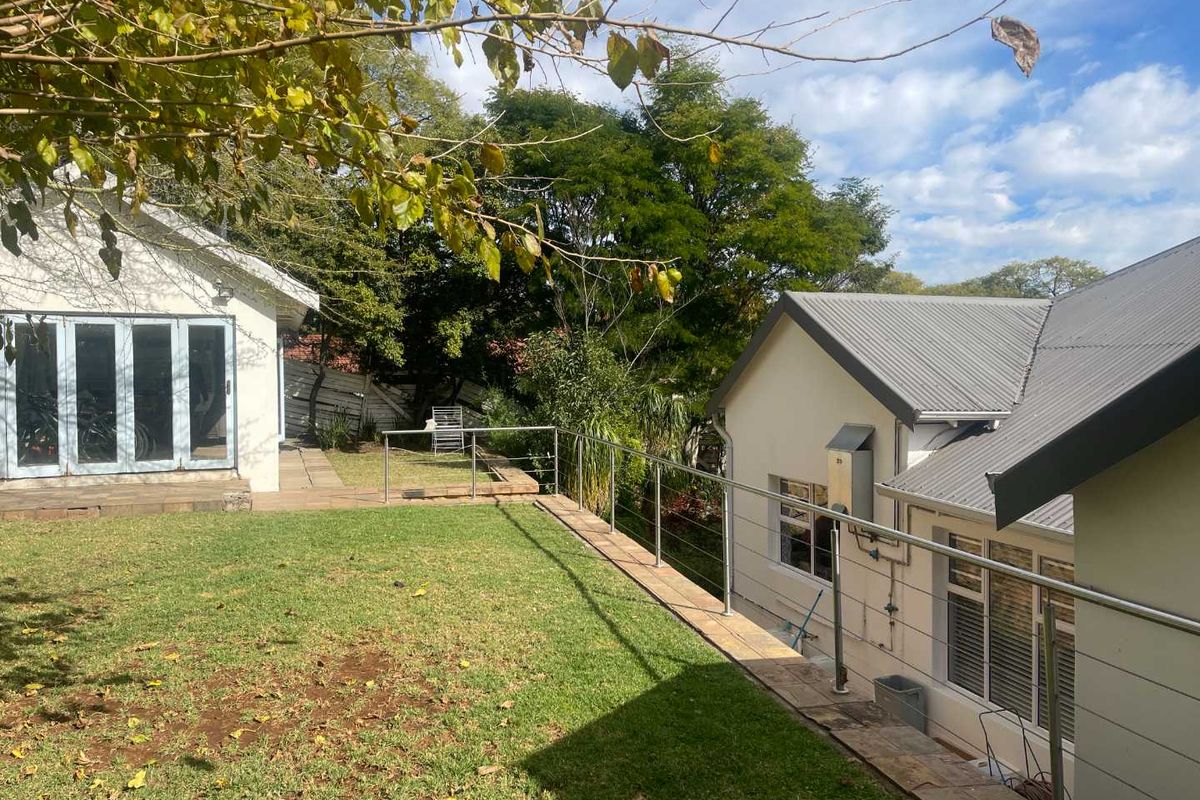 A well-maintained rear garden area featuring a raised lawn, stainless steel balustrade, and views of the adjacent building structures.