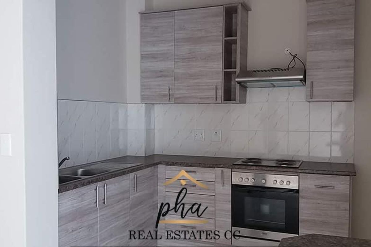 Modern kitchen featuring wood-grain cabinetry, built-in oven, electric hob, stainless steel sink, and tiled splashback.