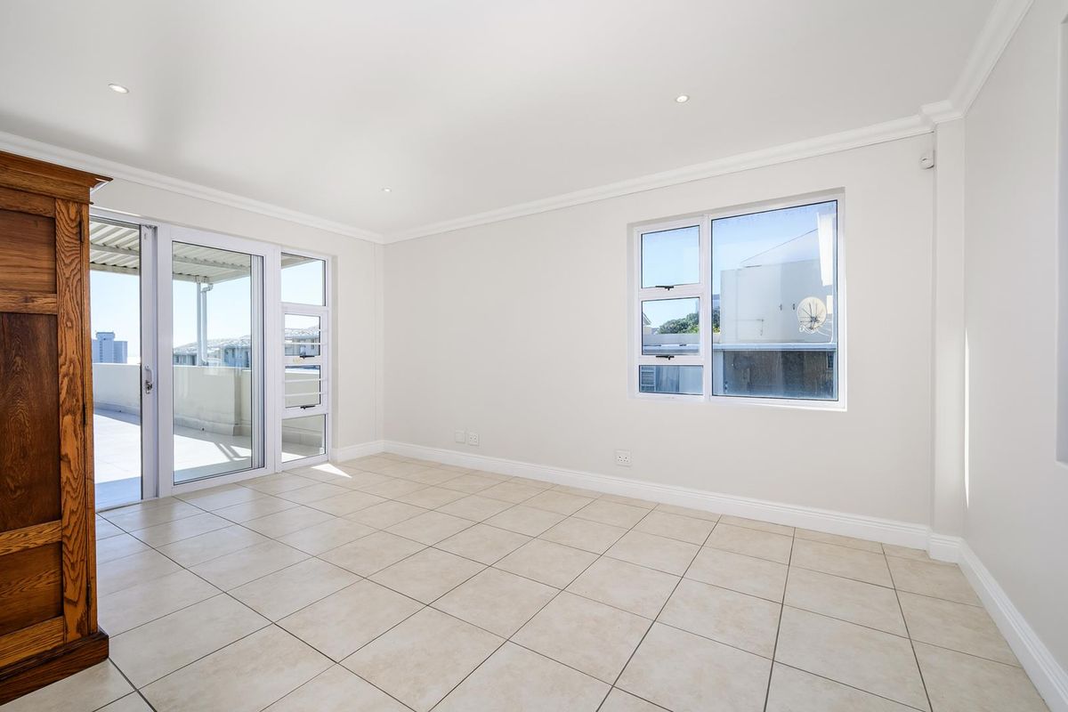 A bright, empty living area featuring neutral tiled flooring, recessed lighting, and direct access to an outdoor balcony through sliding glass doors.