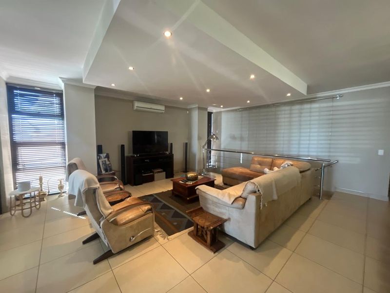 Spacious living room featuring a recessed ceiling with downlights, tiled flooring, and a split-system air conditioner, offering a comfortable and functional layout.