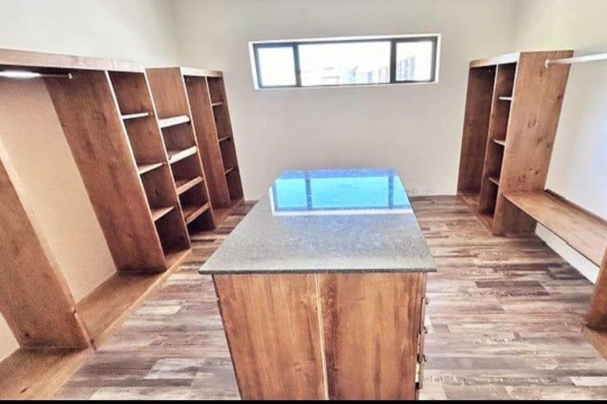 A spacious walk-in closet featuring custom built-in wooden cabinetry, shelving units, and a central island with a stone countertop.