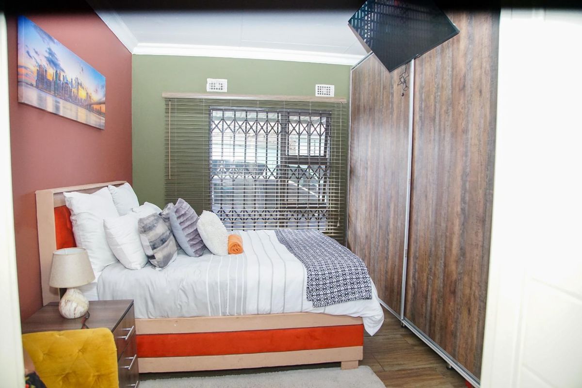 A bedroom featuring built-in sliding door wardrobes, a window with security bars and blinds, and crown molding.