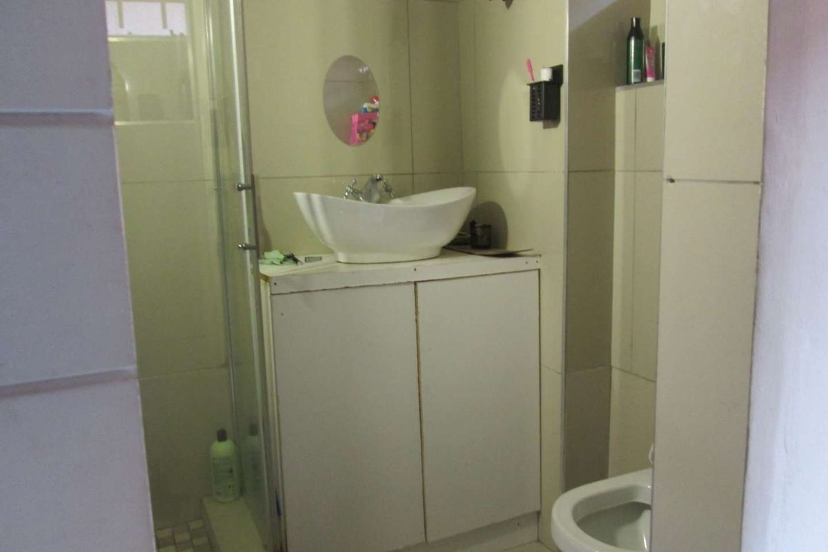 A compact bathroom featuring a vessel sink on a vanity cabinet, a glass shower enclosure, and a toilet with neutral wall and floor tiling.