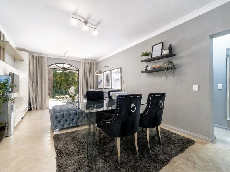 A bright, open-plan living and dining area featuring polished concrete floors, crown molding, and a large arched glass door leading to the outdoors.