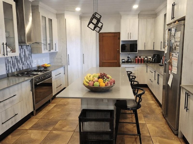 Modern kitchen featuring a central island, stone countertops, gas stove with extractor, and ample built-in cabinetry with a light wood-grain finish.